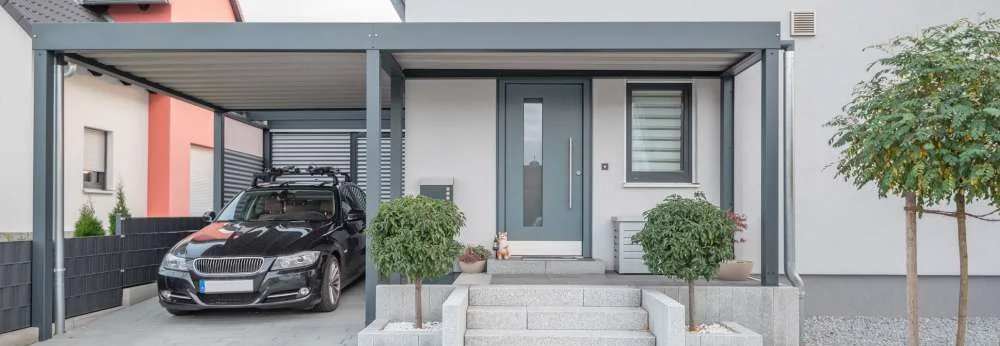 Modernes Haus mit einem grauen Carport und einem schwarzen Auto.